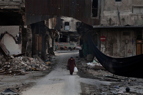 syria aleppo woman walking through street next to long black cloth that separates the area from assad troops